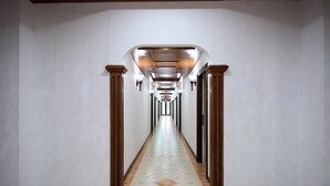 A long, narrow hallway with a patterned floor, wooden columns, and a ceiling with recessed lighting. - Belau Almond Hotel (Malakal Island)