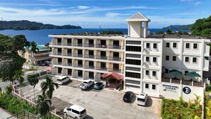 A multi-story hotel with a rooftop terrace, parking area, and a view of the sea. - Belau Almond Hotel (Malakal Island)