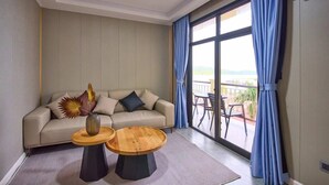 A modern living room with a sofa, two round wooden tables, and a view of the outdoors through large windows. - Belau Almond Hotel (Malakal Island)