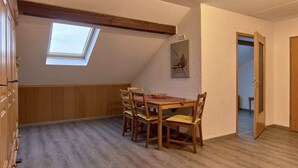 Un coin repas avec une table et des chaises en bois, une lucarne et un tableau au mur.