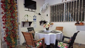 A dining area with a table set for two, chairs, a TV mounted on the wall, a decorative plant, and a window with decorative bars.