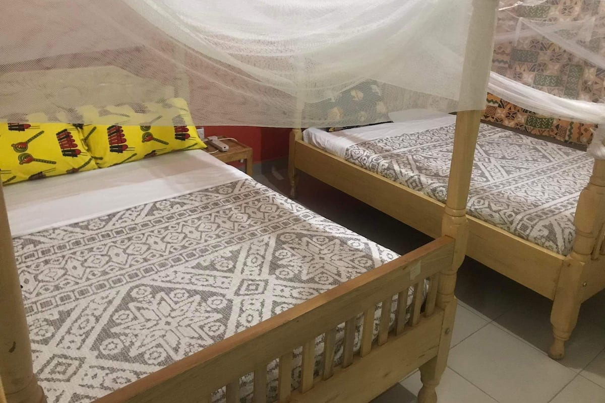 A room with two wooden beds, each with patterned bedding and a white canopy.