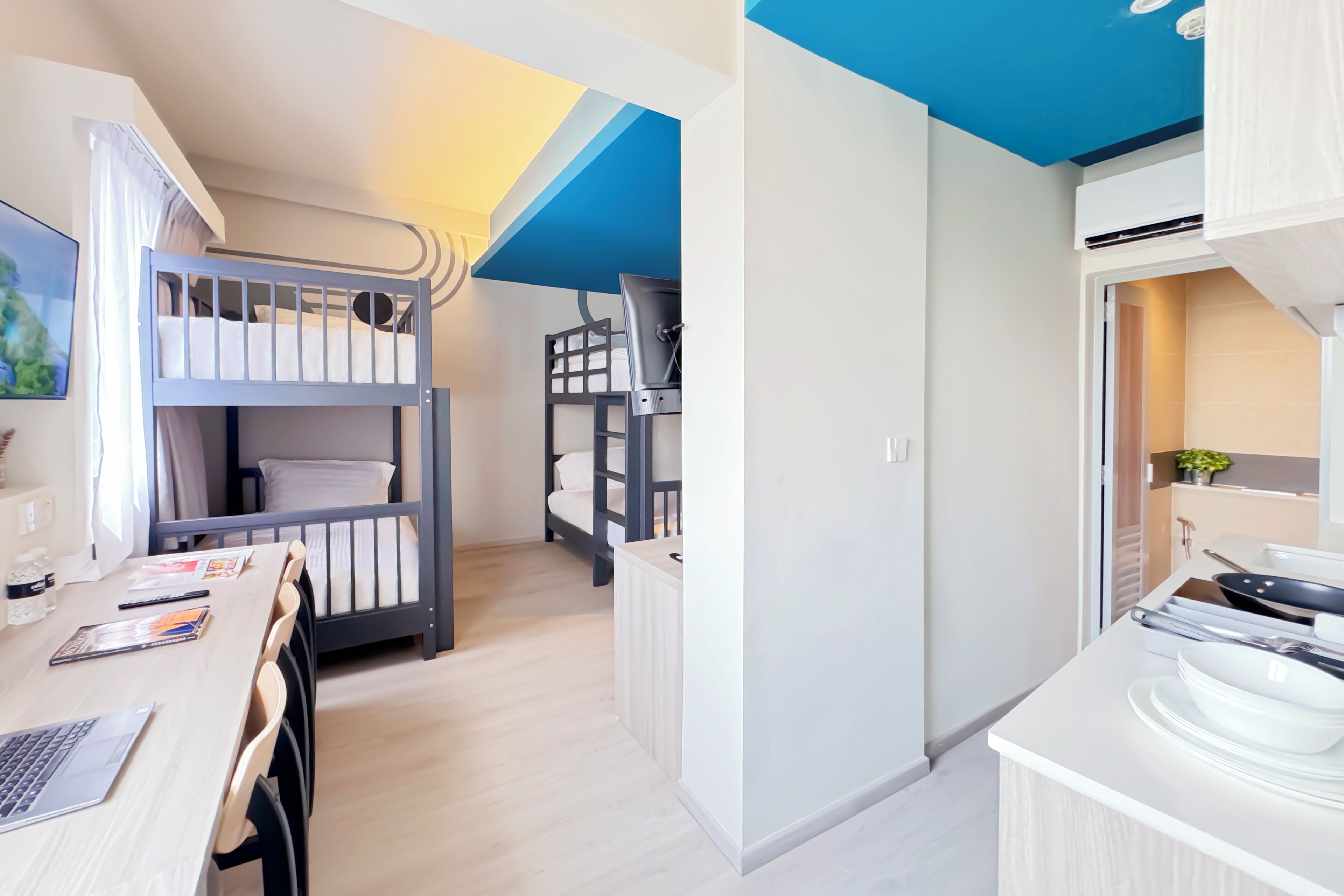 Una habitación moderna con literas, un escritorio con una computadora portátil y una kitchenette.
