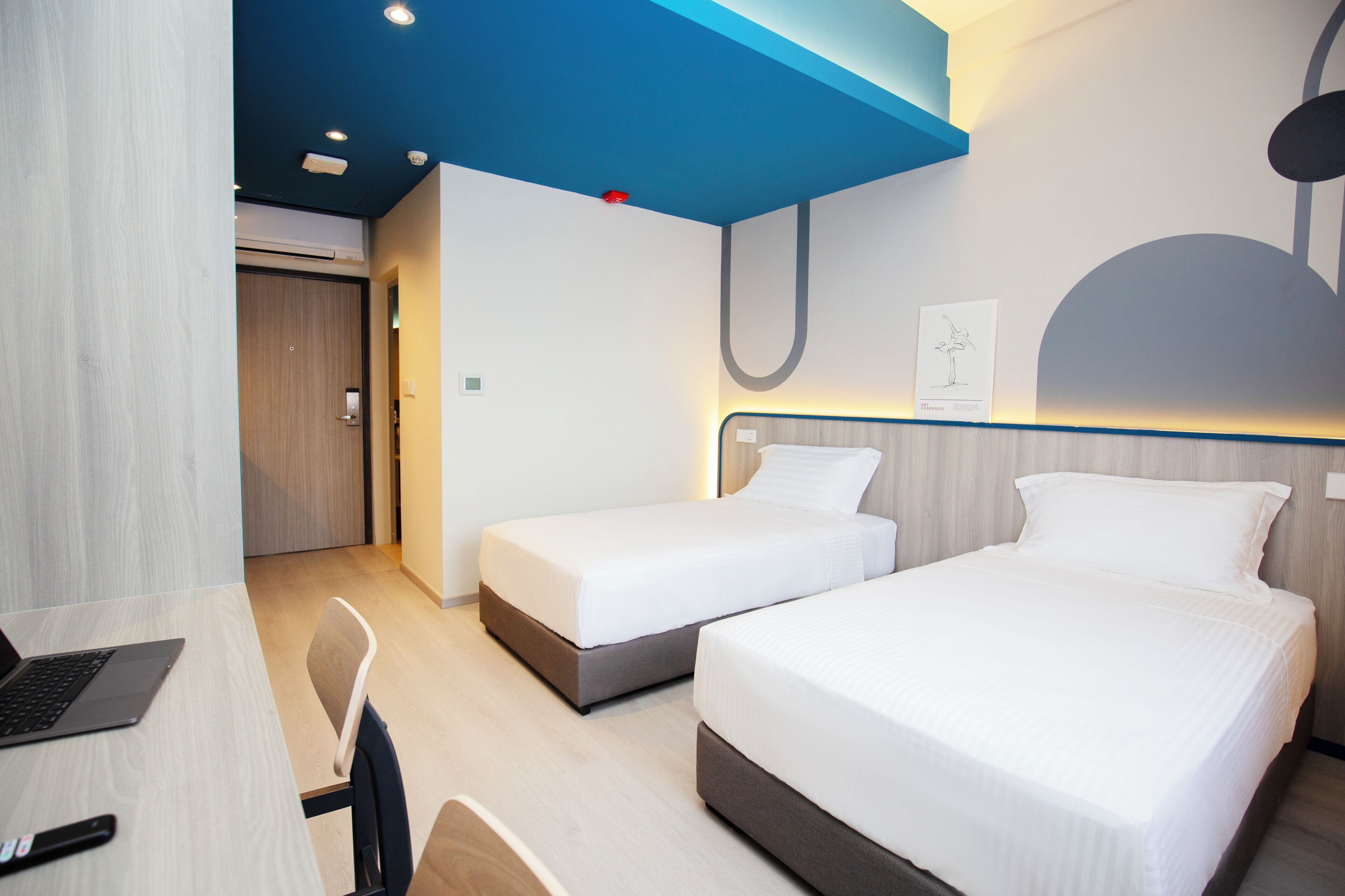 A hotel room with two beds, a desk with a laptop, and a chair.