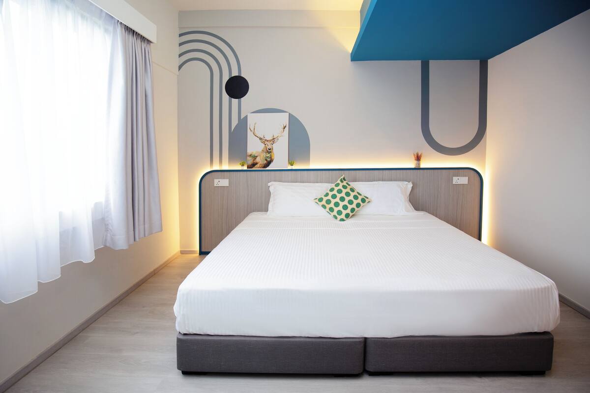 Een moderne hotelkamer met een groot bed, een hoofdbord met ingebouwde verlichting, een kunstwerk van een herten aan de muur en een minimalistisch design.