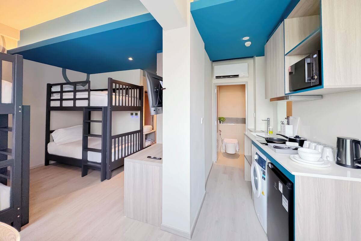 Een compacte hotelkamer met stapelbedden, een kitchenette en een wasmachine.