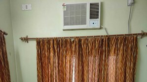 A hotel room with a bed, two pillows, a curtain, an air conditioner, and a power outlet. - Hotel Jamna Vilas (Bikaner)