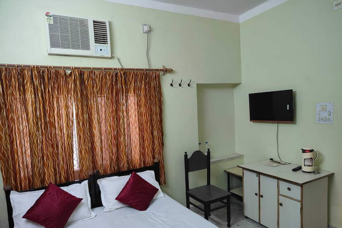 A hotel room with a bed, a desk with a chair, a television, and an air conditioning unit.