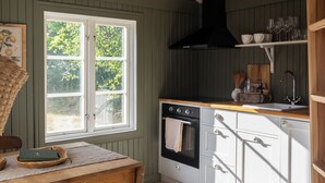A kitchen with wooden beams, a window, a stove, and white cabinets. - Cozy vacation home on Öland, close to nature and the sea (Kalmar län)