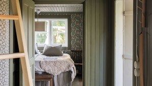 A narrow hallway leading to a bedroom with a bed, a window, and a wooden ceiling. - Cozy vacation home on Öland, close to nature and the sea (Kalmar län)