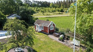 A red house with a white porch, surrounded by a green field and trees. - Cozy vacation home on Öland, close to nature and the sea (Kalmar län)