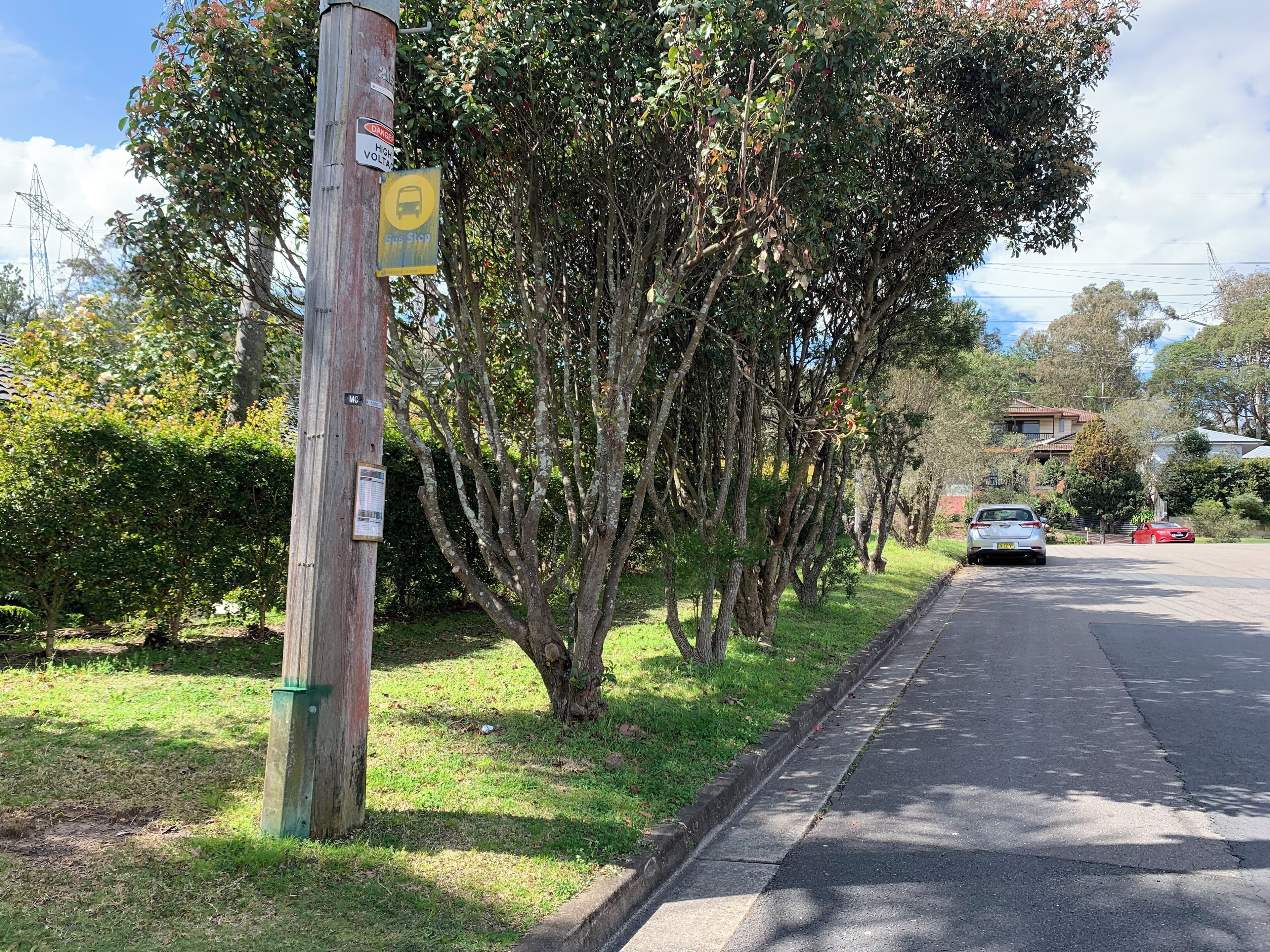 Una calle con una señal de parada de autobús, un poste de electricidad con varias señales y árboles a lo largo de la vía.