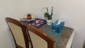 Ein Esstisch mit einem Stuhl, einer kürbisförmigen Kerze, einer Tafel Schokolade, einer Topfpflanze und einer Taschentuchbox.