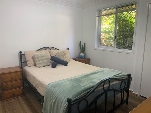 A bedroom with a bed, a nightstand, a dresser, and a window with a view of greenery.