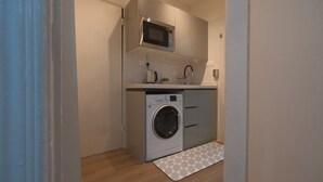 A compact kitchen with a built-in washing machine, a microwave, and a sink. - 2-bedroom apartment IKEA style (Riyadh)