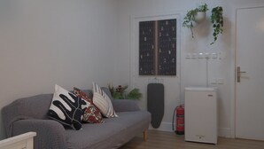 A living room with a grey sofa, patterned cushions, a small plant, a fire extinguisher, and a white door with a blackboard. - 2-bedroom apartment IKEA style (Riyadh)