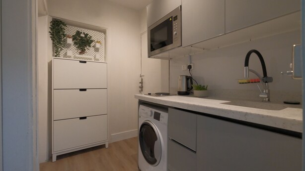 A compact kitchen with a built-in microwave, a washing machine, and a sink with a faucet. - 2-bedroom apartment IKEA style (Riyadh)