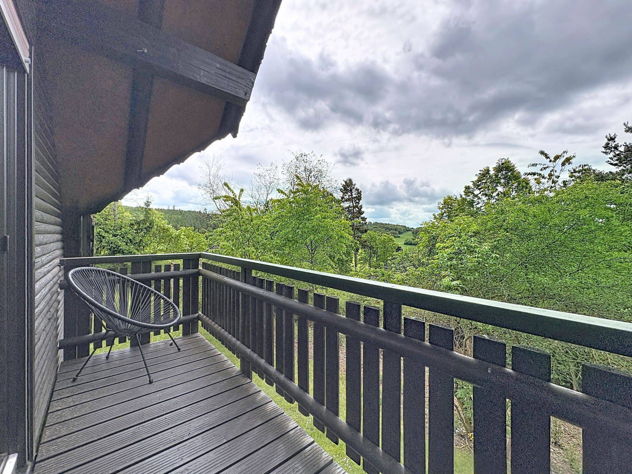 Una terraza de madera con una silla metálica, con vista a un área boscosa.