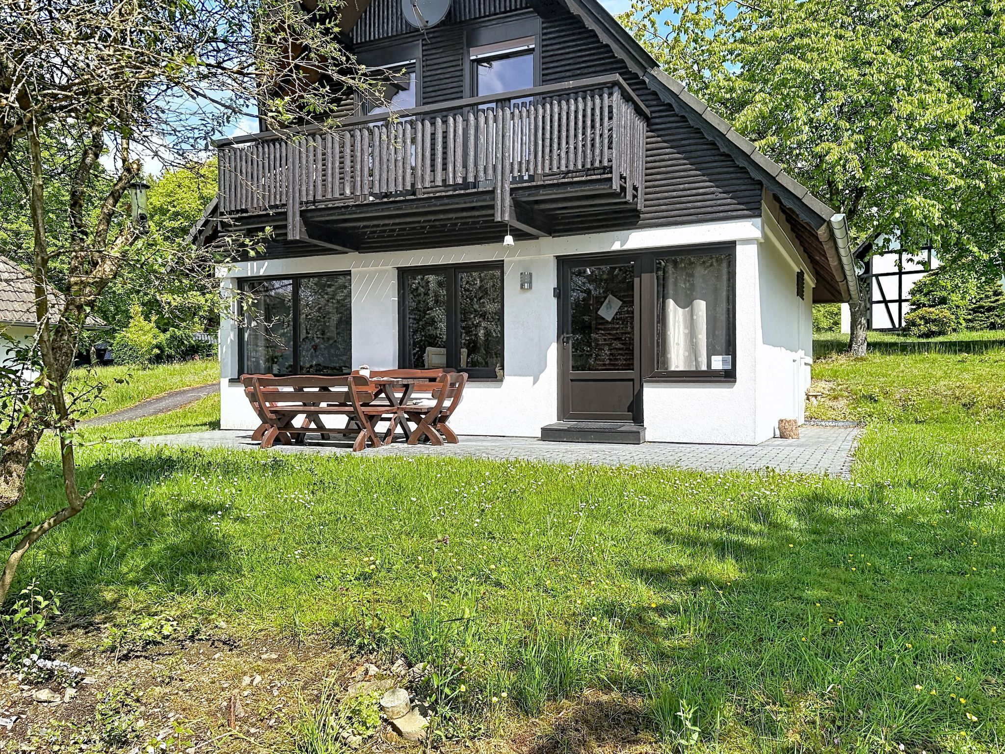 Ein zweistöckiges Haus mit Balkon, einem Esstisch mit Stühlen und einem kleinen Garten.
