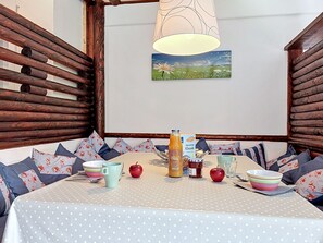 Uma área de estar acolhedora com uma mesa posta para o pequeno-almoço, com toalha de mesa de bolinhas, paredes de madeira e um quadro de um campo.