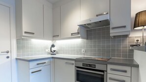 A modern kitchen with white cabinets, a built-in oven, and a countertop with a kettle. - Zandloper III with terrace by Interhome (Bredene)
