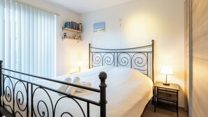 A neatly made bed with a metal headboard, a bedside table with a lamp, and a shelf with books. - Zandloper III with terrace by Interhome (Bredene)
