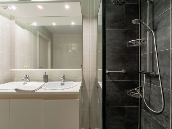 Casa de banho moderna com chuveiro de vidro, lavatório com espelho e um porta-toalhas.