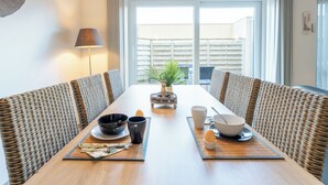 A dining area with a long table, wicker chairs, and a view of the outside. - Zandloper III with terrace by Interhome (Bredene)