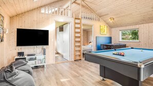Un interior de madera con una mesa de billar, un televisor y una escalera que sube a un nivel superior.