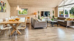 Un amplio espacio de sala con techo de madera, una mesa de comedor con sillas, un sofá y un televisor.