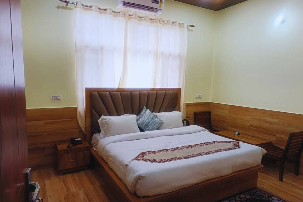 A bedroom with a wooden headboard, a bed with white bedding, a bedside table, a chair, and a small wooden nightstand.