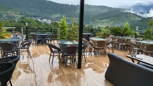 An outdoor patio with tables and chairs, overlooking a mountainous landscape. - Hotel Shani - Punjabi Rasoi (Palampur)