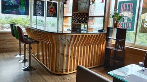 A bar area with wooden accents, bar stools, and a view of greenery outside. - Hotel Shani - Punjabi Rasoi (Palampur)