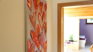 A hallway with a large abstract painting on the wall, a round table with a plant, and a glimpse of a room with a bed and a purple wall. - Ferienwohnung in Freital, Dresden (Freital)