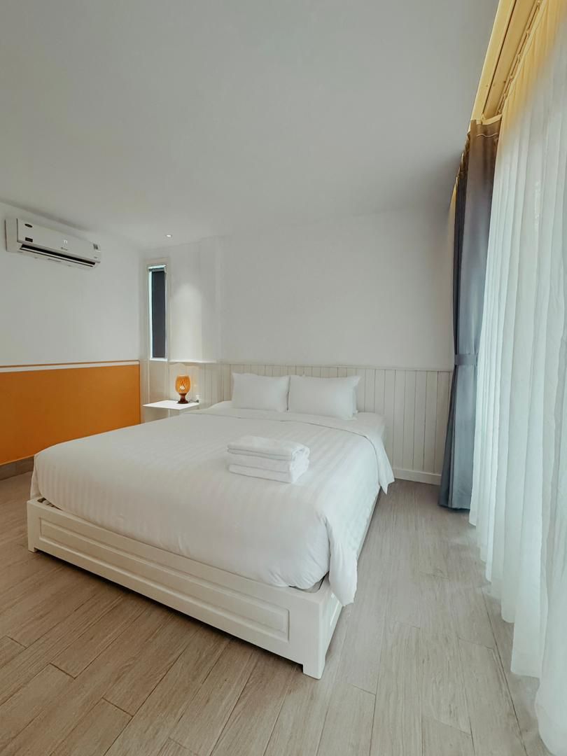 Una cama grande con ropa blanca, una mesita de noche con lámpara y una ventana con cortinas.