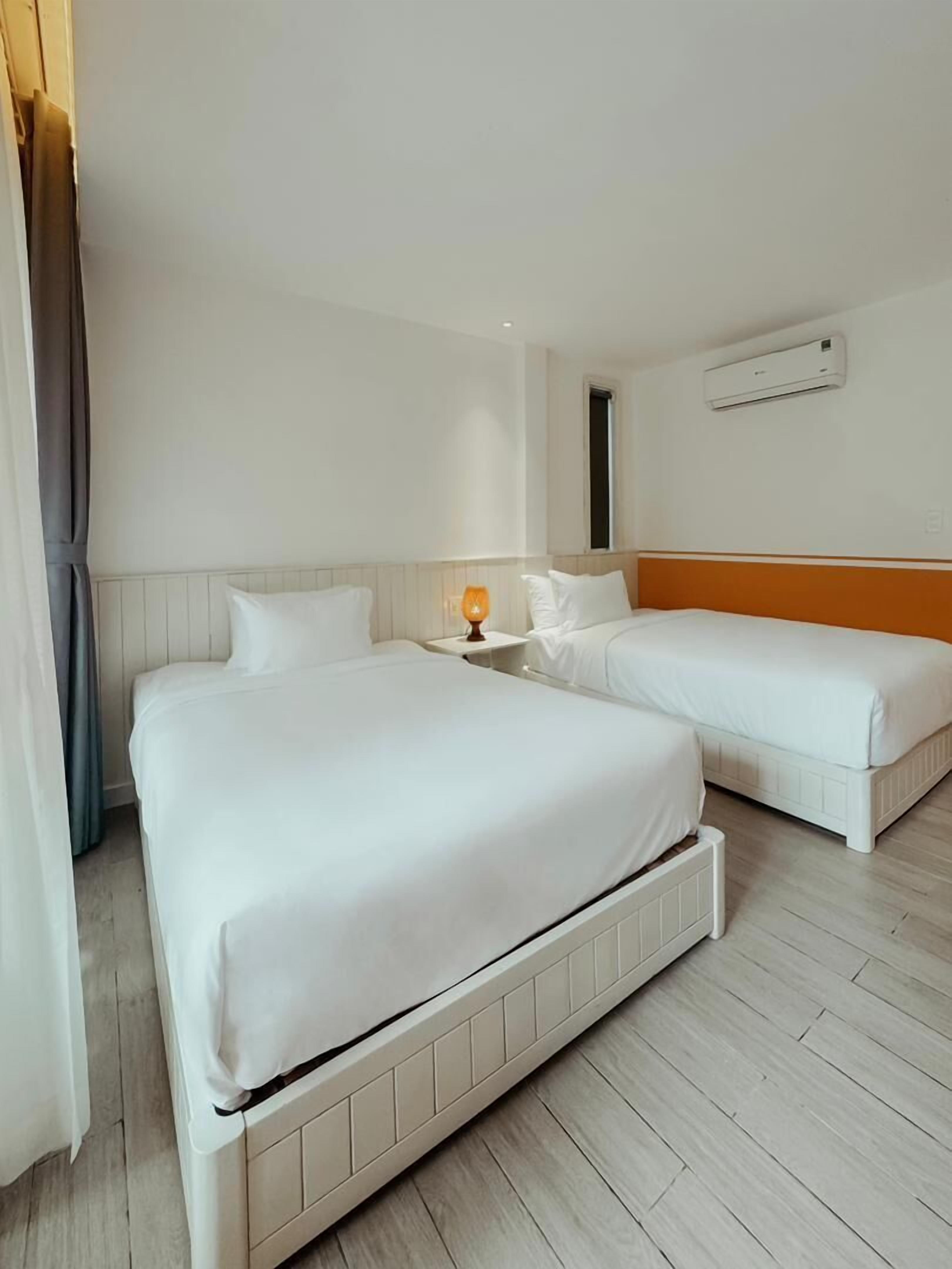 A hotel room with two beds, a nightstand, an air conditioning unit, and a window with curtains.