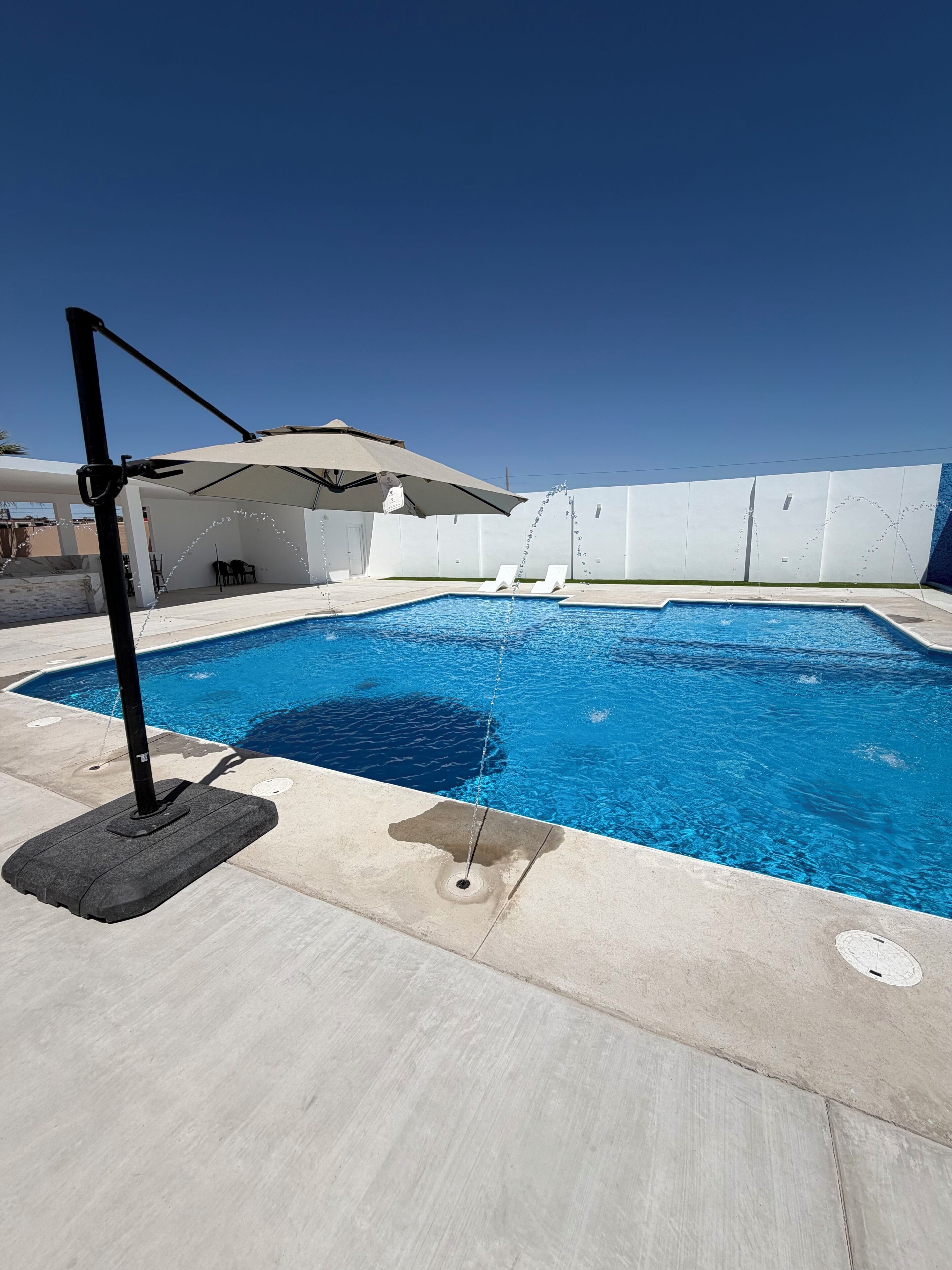 A swimming pool with a sun umbrella, lounge chairs, and a covered seating area.