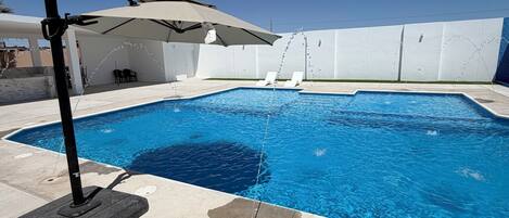 A swimming pool with a sun umbrella, lounge chairs, and a covered seating area.