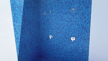 Un baño moderno con pared de ducha de mosaico azul, techo blanco y suelo de césped artificial verde.