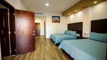Habitación de hotel con dos camas, suelo de madera, un cuadro en la pared y una puerta.