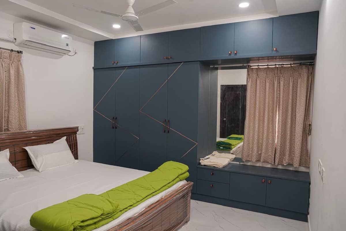 A bedroom with a bed, a wardrobe, a mirror, and an air conditioning unit.