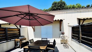 En udendørs terrasse med et bord, stole, en stor parasol og en grill.