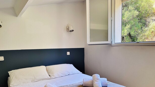 Et hotelværelse med en seng, et vindue med udsigt til grønne områder, en vægmonteret lampe og en stikkontakt.