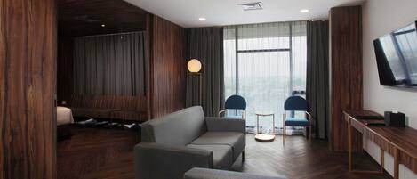 Una habitación de hotel moderna con un sofá, dos sillones, un televisor y suelo de madera.