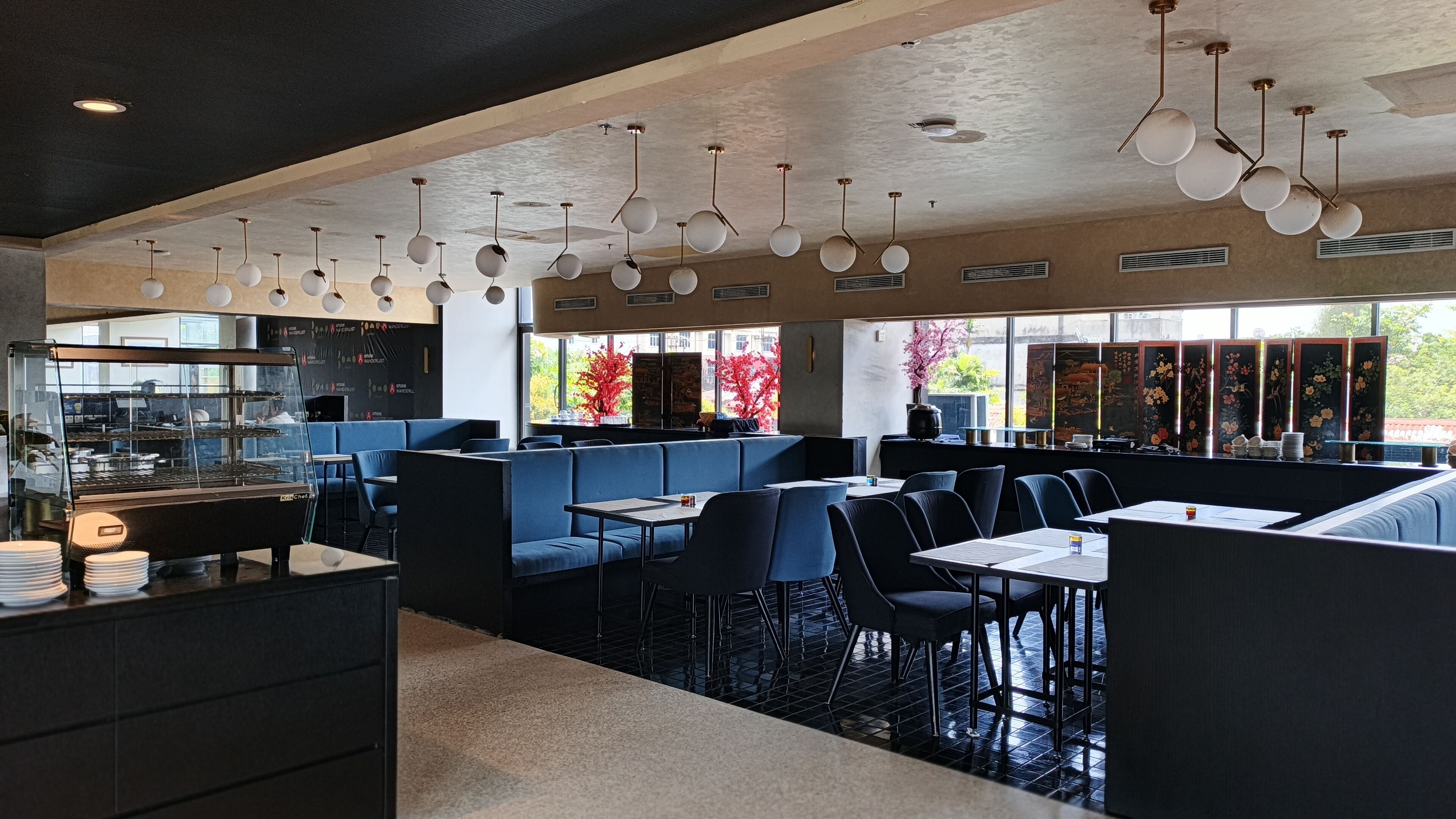 Un interior de restaurante moderno con zona de cocina, disposición de mesas y detalles decorativos.