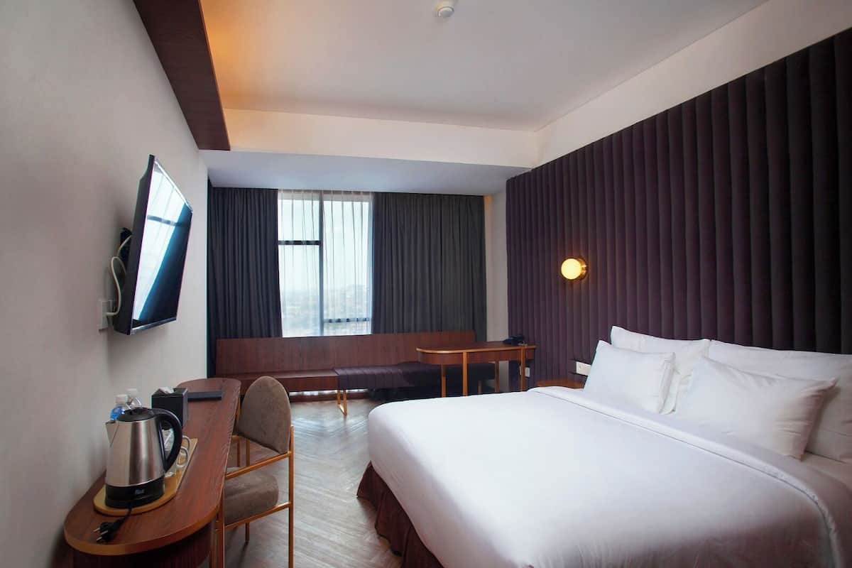 A hotel room with a bed, a desk, a chair, a TV, and a window with curtains.