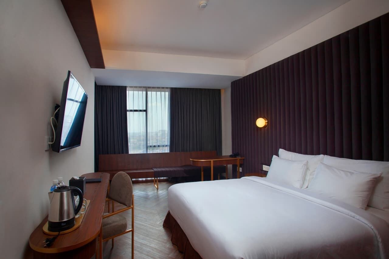 A hotel room with a bed, a desk, a chair, a television, and a window with curtains.