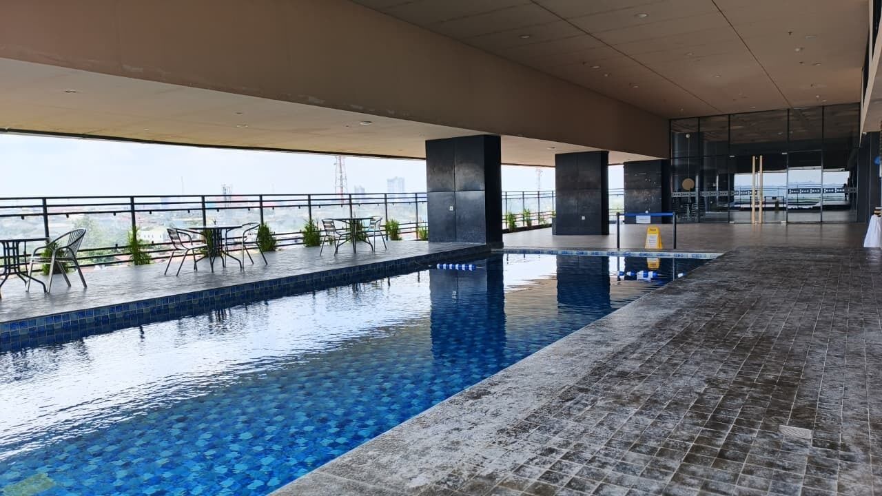An indoor swimming pool with a tiled floor, seating area with chairs, and a view of the cityscape.