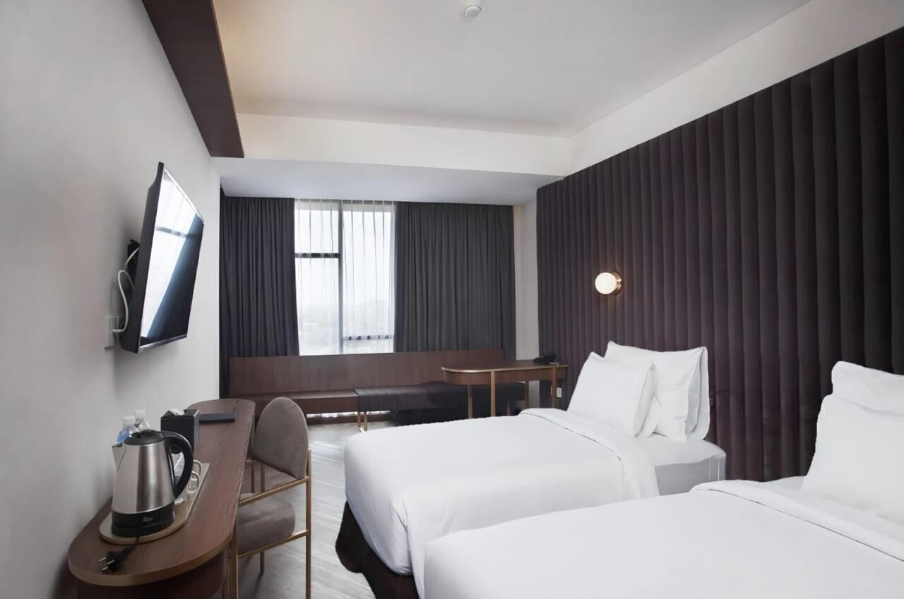 Une chambre d’hôtel avec deux lits, un bureau, une chaise, une télévision et une fenêtre avec des rideaux.