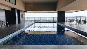 Una piscina en la azotea con suelo de baldosas, sillas de metal y barandilla.